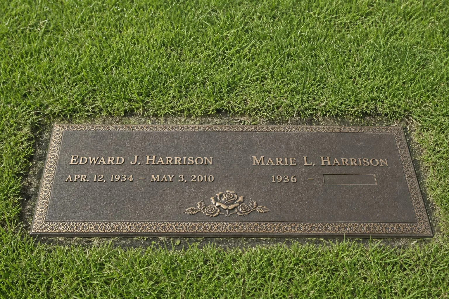 A flush bronze grave marker set level with mown cemetery lawn, showing two names, one with complete dates and one with a birth year and blank space, with a s...